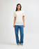 A plain cream tri-blend t-shirt is worn with blue denim pants, featuring a simple design and a logo.