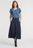 A woman wears a light blue top and a long navy skirt with buttons and pockets. The outfit is stylish and modern.