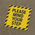 A yellow floor decal sticker with black striped edges and text instructing to "MIND YOUR STEP."