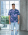 A man stands in a modern space wearing a purple and navy tie-dye T-shirt and ripped jeans. The shirt features a logo.