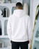 A white hoodie is worn by a person seen from the back, with a styled interior in the background.
