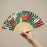 A bamboo hand fan featuring a vibrant floral and leaf design in red, orange, and green hues.