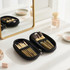 A black case containing nine makeup brushes with gold details, placed on a vanity beside a mirror and various beauty products.