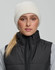 A person wearing a cream-coloured roll-up cable knit snug beanie with a black vest over a grey top.