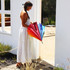 A woman in a white dress holds a vibrant rainbow-coloured Iris Umbrella outside a white building.