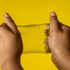A pair of hands stretching a translucent yellow jelly cube sensory toy against a bright yellow background.