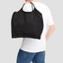A black nylon shopper bag is being carried on the shoulder of a person wearing a white t-shirt.