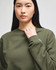 A green crewneck sweatshirt displayed on a model, featuring a small logo on the arm.
