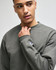 A grey crewneck sweatshirt is worn by a model, featuring a logo on the sleeve.