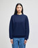 A navy adult crewneck sweatshirt is worn by a model, featuring a logo on the sleeve. The model pairs it with denim jeans.