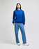 A woman wearing a bright blue crewneck sweatshirt paired with light blue jeans and white sneakers.