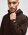 A brown pullover hooded sweatshirt featuring a logo on the sleeve. The model is wearing the hoodie.