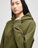 A woman models an olive green hooded sweatshirt with a logo on the sleeve.
