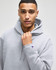 A grey hooded sweatshirt with a front pocket and a logo on the sleeve, modelled by a person.