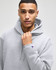 A grey hooded sweatshirt featuring a logo, with a male model wearing it and holding the hood.