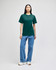 A model wears a green Champion adult short-sleeve t-shirt paired with light blue jeans and white sneakers.