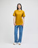 A model wearing a mustard yellow Champion adult short-sleeve T-shirt paired with blue jeans. The shirt features a logo.