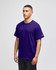 A purple Champion short-sleeve T-shirt worn by a model standing against a plain background. It features a logo on the sleeve.