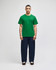 A green Champion adult jersey short sleeve t-shirt displayed on a model with navy blue trousers. The shirt features a logo.