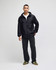 A black full-zip anorak jacket stands on a model, styled with a white shirt and dark pants. The jacket features a logo.