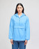 A packable anorak jacket in sky blue, featuring a front pocket and a hood, worn by a model standing upright.