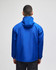A blue packable anorak jacket with a hood, featuring a logo, worn from the back.