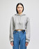 A grey cropped hoodie with a drawstring hood, featuring a logo on the sleeve, paired with blue jeans.