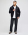 A model wearing a black full-zip hooded sweatshirt over a white t-shirt, paired with dark trousers and sneakers.