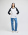 A black and white raglan baseball t-shirt paired with blue jeans, worn by a model standing against a neutral background.