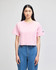 A pink cropped short sleeve t-shirt with a logo on one sleeve, paired with blue jeans.
