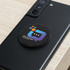 A black magnetic badge with a colourful logo sits on the back of a smartphone, placed on a wooden surface.