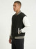 A men's unisex wool blend varsity jacket in black with white sleeves and striped cuffs, featuring a logo on the chest.