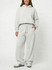 A model wearing unisex wide leg fleece pants in light grey, paired with a matching hoodie. The outfit features a casual style.