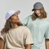 A grey cap and a white cap worn by two models, paired with casual t-shirts in muted colours.