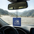 A blue car air freshener hanging from a rearview mirror, featuring a logo and set against a mountain backdrop.