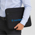 A black neoprene laptop sleeve with a logo, held by a person in a light blue shirt.