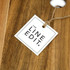 An acacia serving board with a natural wood finish and a tag attached, featuring branding.