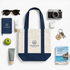A mini canvas tote in navy and cream, surrounded by sunglasses, a camera, skincare products, and a notebook.