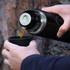 A black 750ml vacuum flask is being poured into a black cup, surrounded by a natural background.