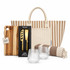 A striped tote bag, a wooden cheese board, a cheese knife set, two clear glasses, and a patterned blanket.