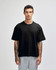 A black unisex heavyweight cotton boxy t-shirt displayed on a model with tattoos, paired with grey trousers.