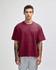 A maroon heavyweight cotton unisex boxy t-shirt displayed on a model with tattoos, paired with grey pants.