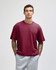 A maroon unisex boxy t-shirt displayed on a model, paired with grey sweatpants. The shirt features a logo.