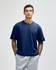 A navy unisex boxy T-shirt featured on a model, paired with grey sweatpants. The shirt has a branding logo.