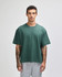A green heavyweight cotton unisex boxy T-shirt displayed on a model with tattoos, paired with grey pants.