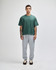 A unisex boxy t-shirt in green, paired with grey sweatpants, worn by a model standing against a plain background.