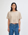 A cropped boxy t-shirt in a neutral beige colour, featured on a model wearing blue jeans. The shirt has a logo.