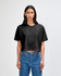 A black heavyweight cotton women's crop boxy t-shirt on a model, paired with blue jeans. It features a logo.