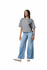 A woman stands in a grey, mid-length boxy top paired with light blue wide-leg jeans, wearing white shoes.