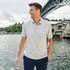 A light grey men's polo shirt with a collar, worn by a man standing by the water, under a bridge.